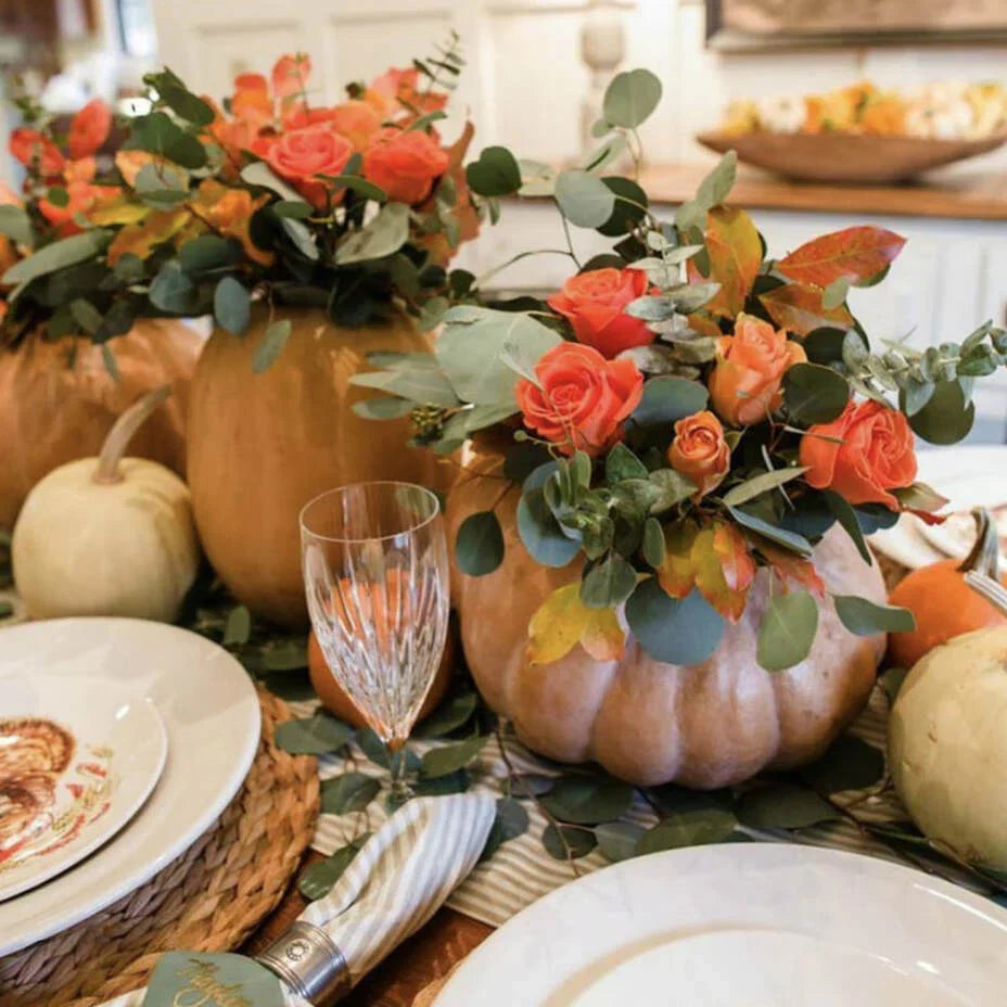 Pumpkins filled with coral color roses and greenery on the Thanksgiving table