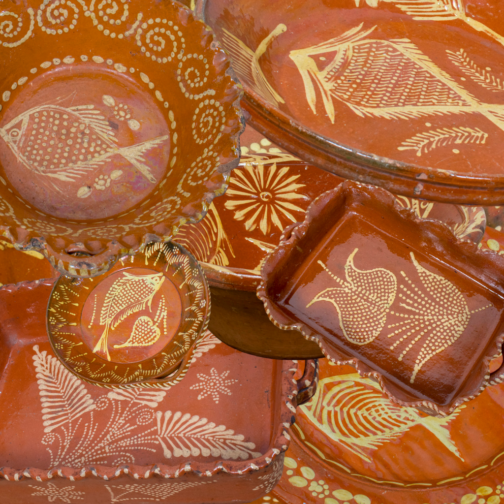 Collection of Portugese red slipware baking dishes with ruffled edges, serving bowls, and serving platters with fish, leaf, and floral motifs
