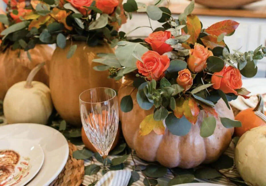 Pumpkins filled with coral color roses and greenery on the Thanksgiving table 