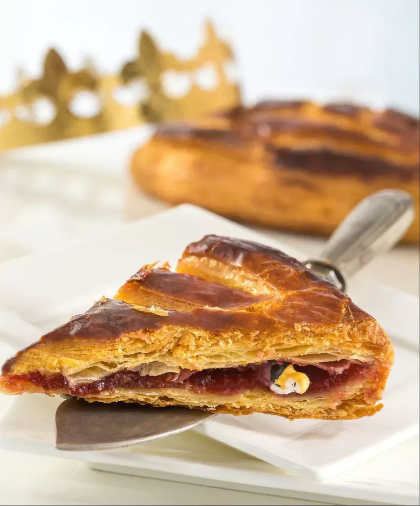 A slice of French galette des rois or king cake with crown and fève showing in the cake slice.