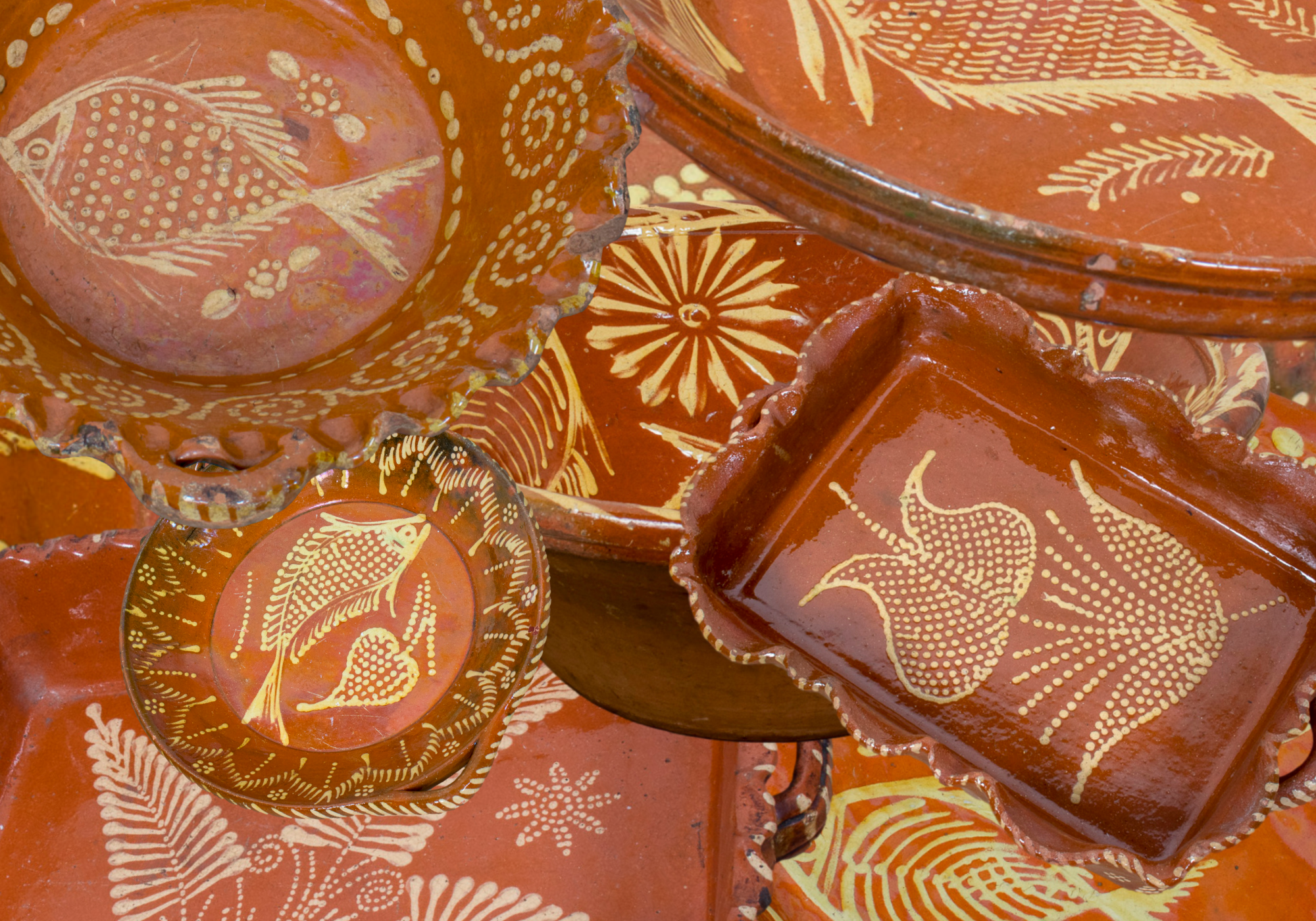 Collection of Portugese red slipware baking dishes with ruffled edges, serving bowls, and serving platters with fish, leaf, and floral motifs 